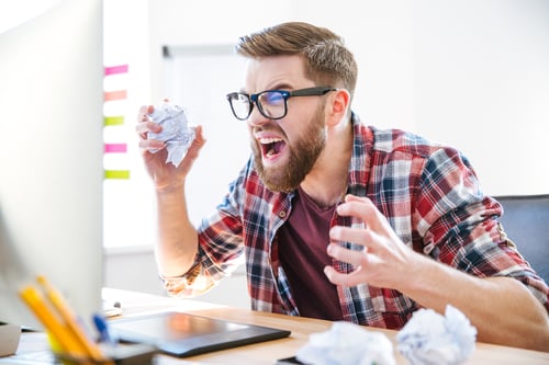 Angry crazy modern designer in glasses with beard yelling and crumpling paper on his workplace-1